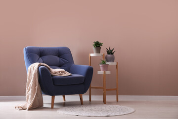 Comfortable blue armchair with blanket and beautiful plants near pink wall indoors