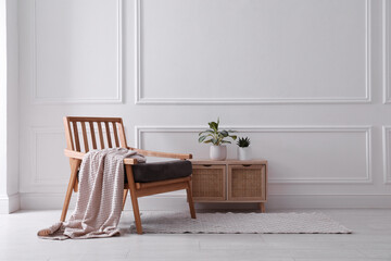 Comfortable wooden armchair with blanket and beautiful plants near white wall indoors