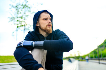 man with arm prosthesis in sports clothing ready for morning workout outdoors. Disabled sport...
