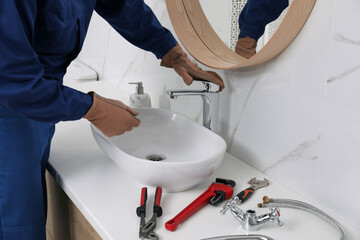 Professional plumber checking water tap in bathroom, closeup