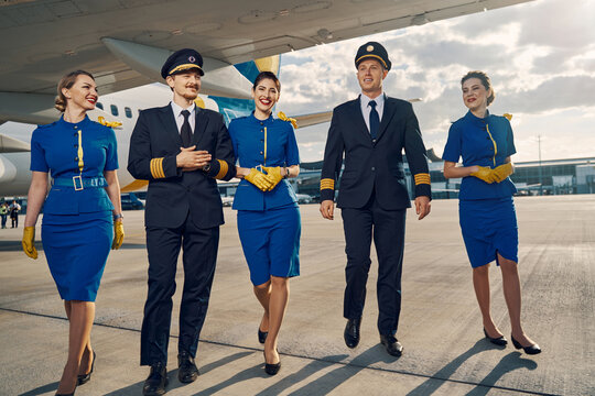 Happy aircrew in uniforms going along the runway