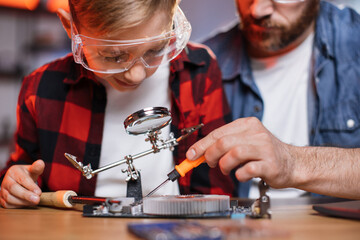 Caucasian man and cute boy using screwdriver, soldering iron and magnifying glass for repairing...