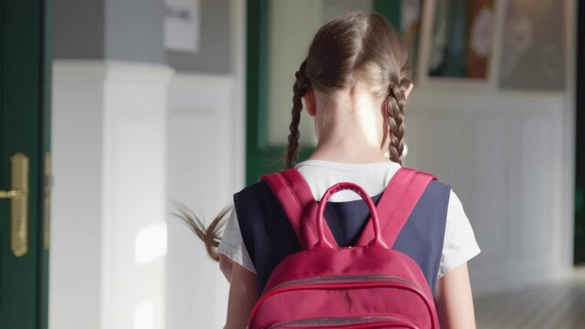 Follow shot of preteen girl with braids and backpack walking in empty school corridor