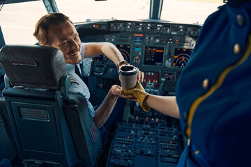 Airline captain being served coffee in the cockpit