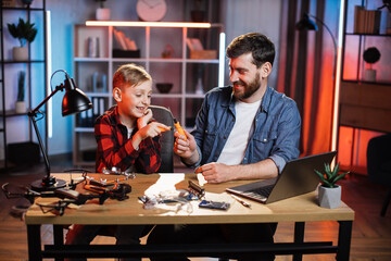 Positive bearded man and little boy playing with screwdrivers while sitting together at home. Young father teaching lovely son about repairing in game form.