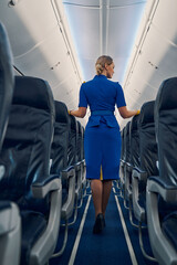 Blonde air hostess in uniform standing in the cabin aisle