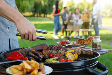 Man cooking meat and vegetables on barbecue grill in park, closeup