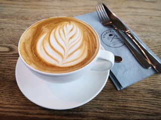 Coffee Latte and a knife and a fork on a wooden cafe table 