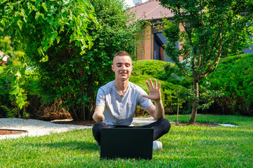 Young smiling guy with amputated arm sits on a lawn in backyard of his house and talking with...