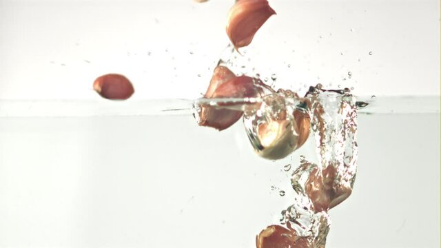 Super slow motion garlic cloves fall under the water on a white background. Filmed on a high-speed camera at 1000 fps. High quality FullHD footage