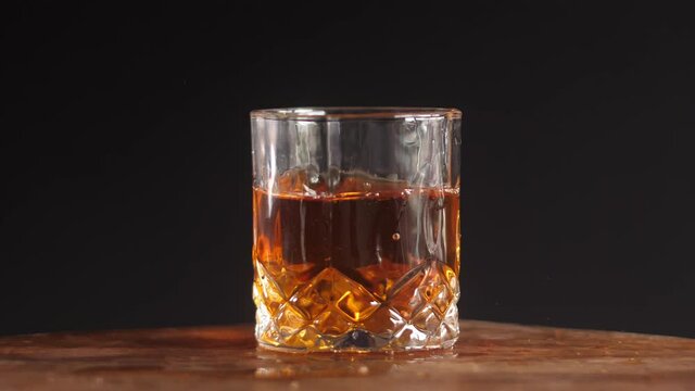 Whiskey glass with ice cube splash in slow motion