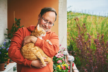 Portrait of middle age man holding cute ginger cat, resting on small cozy balcony - 449415157