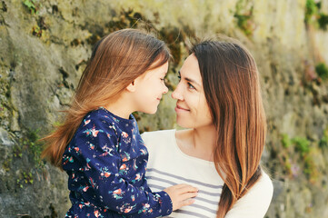 Outdoor portrait of happy young mother holding little daughter in arms, looking at each other