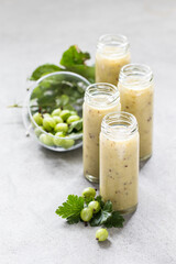 Smoothie made of fresh gooseberries in a tall glass bottle with a straw on a light gray background