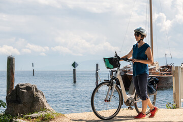 Frau mit Elektro Fahrrad am Bodensee bei schönem Sommer Wetter, genießt und entspannt.