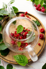 A warm drink on a light background. Berry tea with raspberries and red currants. Tea made from berries in a teapot. Summer still life with leaves and tea. Fresh raspberry harvest