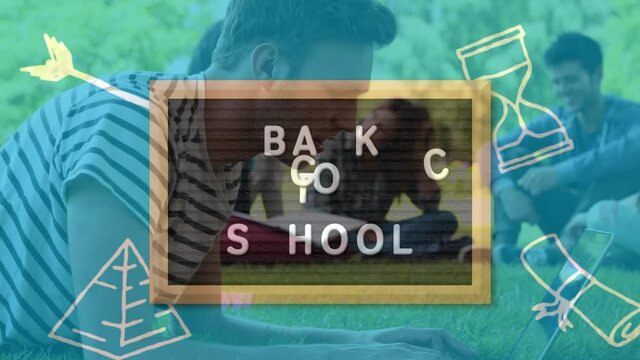 Back to school text on wooden slate against caucasian male student using laptop on the grass