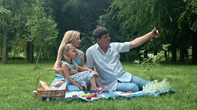 A man takes pictures of himself, a child and a woman at a summer picnic in nature