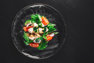 Salad with cucumber, tomato, red onion, pepper, parsley and Feta cheese on black background