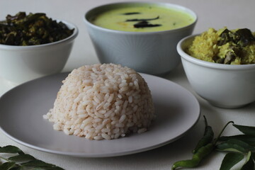 Vegetarian meals prepared in Kerala style. The serving includes boiled red rice, stir fried onions with grated coconut, stir fried okra, tempered buttermilk and poppadum.