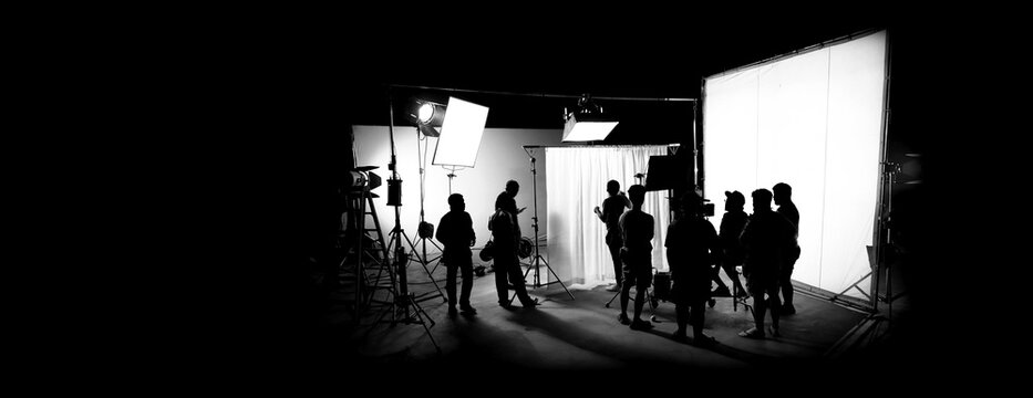Silhouette images of film production. behind the scenes or b-roll of making video commercial movie. Film crew lightman and cameraman working together with film director in studio. Film industry.