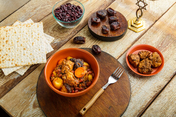 Jewish dish shuttle with meat in a dish on a wooden table near matzo and ingredients.