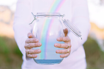 Woman releasing a rainbow over ocean from a glass jar
