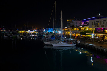 Night view of Limassol in the Marina area. Moored pleasure yachts in front of restaurant lights and vibrant nightlife.