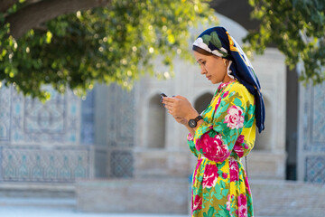 Muslim girl with a scarf on her head at the gate of the old mosque. Bukhara, Uzbekistan. - obrazy, fototapety, plakaty