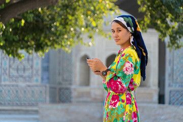Muslim girl with a scarf on her head at the gate of the old mosque. Bukhara, Uzbekistan. - obrazy, fototapety, plakaty