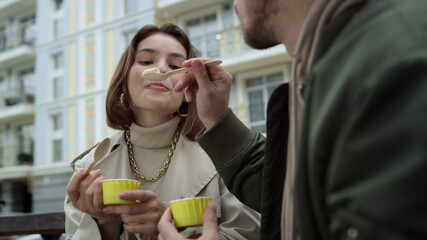 Happy couple enjoying ice cream outdoor. Man feeding woman on urban street.