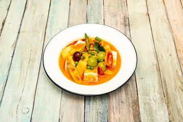 Thai spicy red curry with tofu and fruits on a white enameled metal plate and blue rim