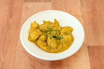 Curry stewed chicken recipe with grated coconut and chives on wooden table