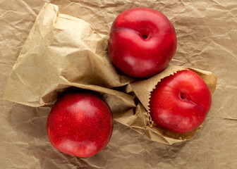 Three organic sweet, red plums on craft paper, close-up, top view.