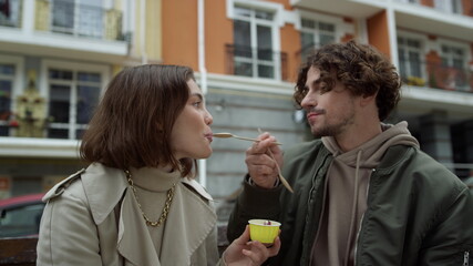 Cheerful couple eating ice cream outdoor. Joyful pair kissing on city street.