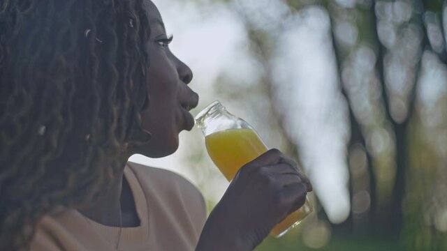 Happy afro-american woman drinking orange juice outdoor, healthy beverage