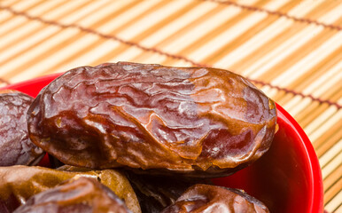 Big luxury dried date fruit in bowls on the bamboo mat, kurma ramadan kareem concept, close up.