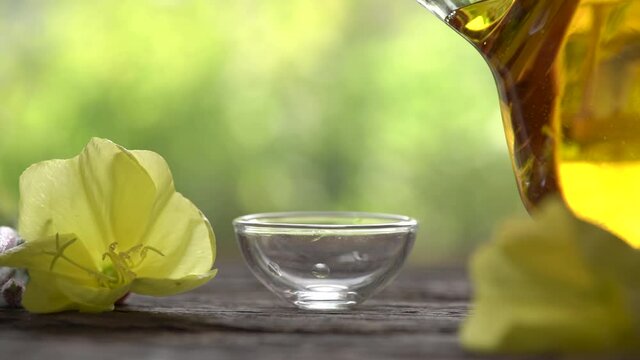 Slow motion of pouring evening primrose oil from a bottle, with fresh Oenothera biennis flowers in the background