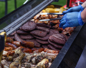 person in blue gloves serves range of grilled meat from a barbecue with tongs