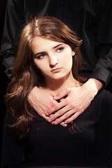 Naklejka premium Portrait of a young girl, male hands lie on her shoulders, black background