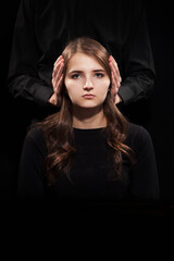Portrait of a girl on a black background with male hands covering her ears