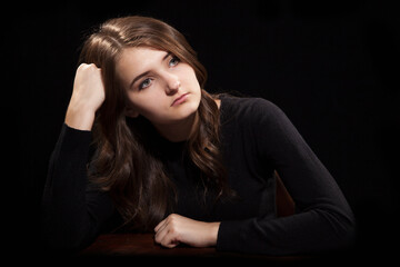 Portrait of a young girl sitting at the old table on a black background