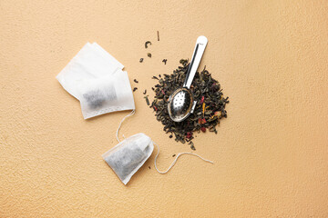 Tea bags and strainer with dry leaves on color background