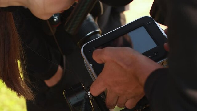 Director of photography shows director footage on display of digital cinema camera during shooting of movie. DOP, operator. Production. Stage, scene. On set. Cinematography and videography. Rental