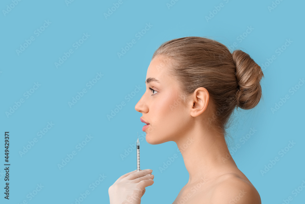 Wall mural Young woman receiving filler injection in lips against color background