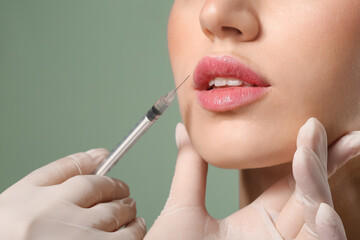 Young woman receiving filler injection in lips against color background, closeup