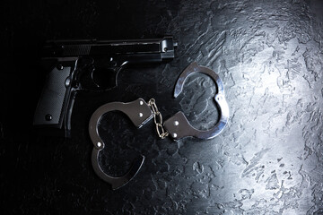 Black steel gun and Police metal real handcuffs lie on the black background. Private detective...