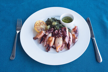 Grilled squid with potatoes and spinach on a white plate. Dish with seafood. Romantic dinner at a fish restaurant in the resort of Montenegro. Travel by Montenegro.