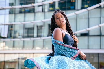 Black teenage girl with afro braided hair, looking at the camera. With a office buildings...
