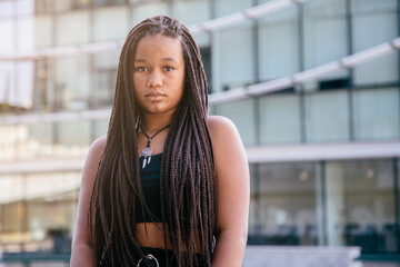 Black teenage girl with afro braided hair, looking at the camera with serious expression. With a...